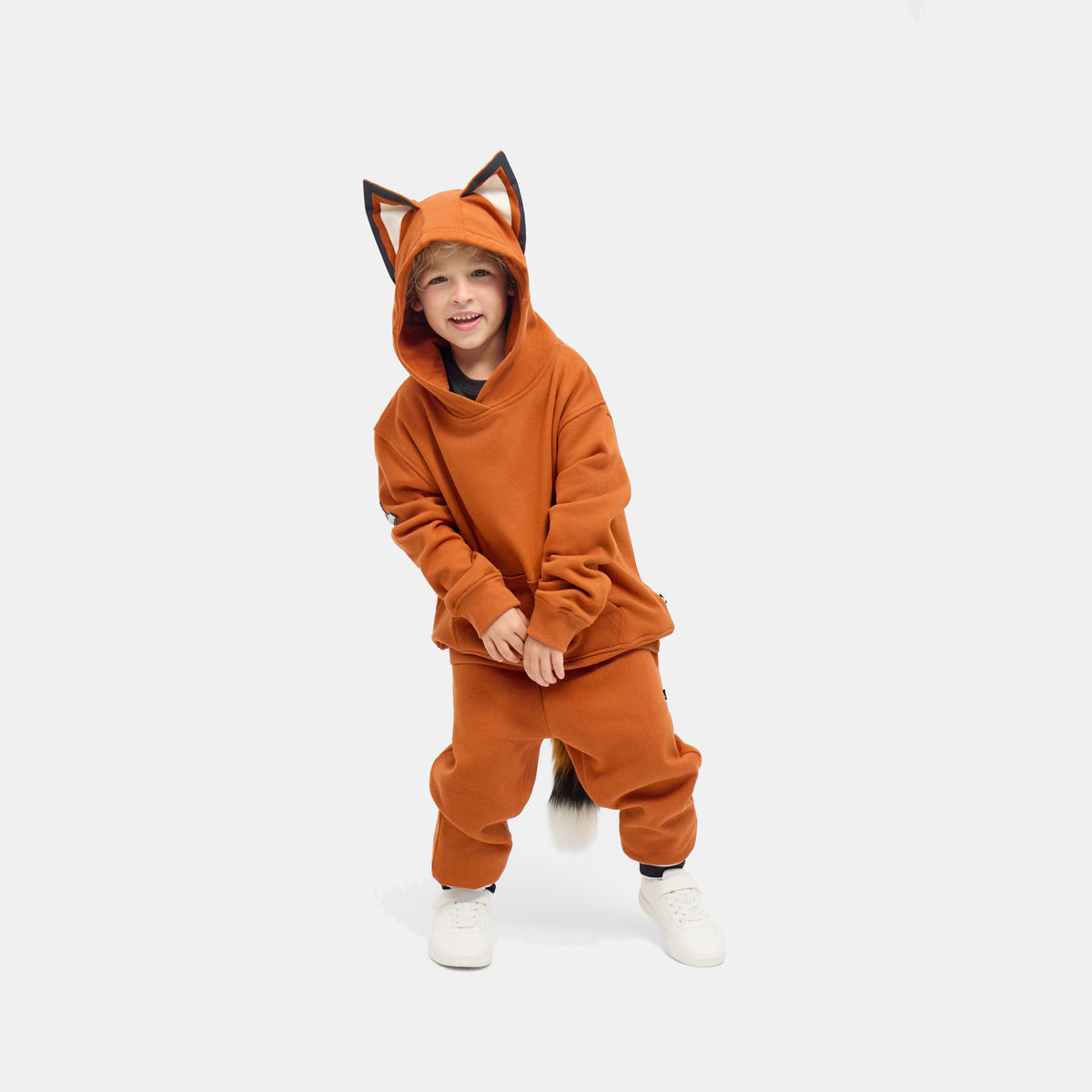 Child crouching in the rust-orange FOXDO Sweatsuit, hood up with fox ears, hoodie and joggers worn as a set.
