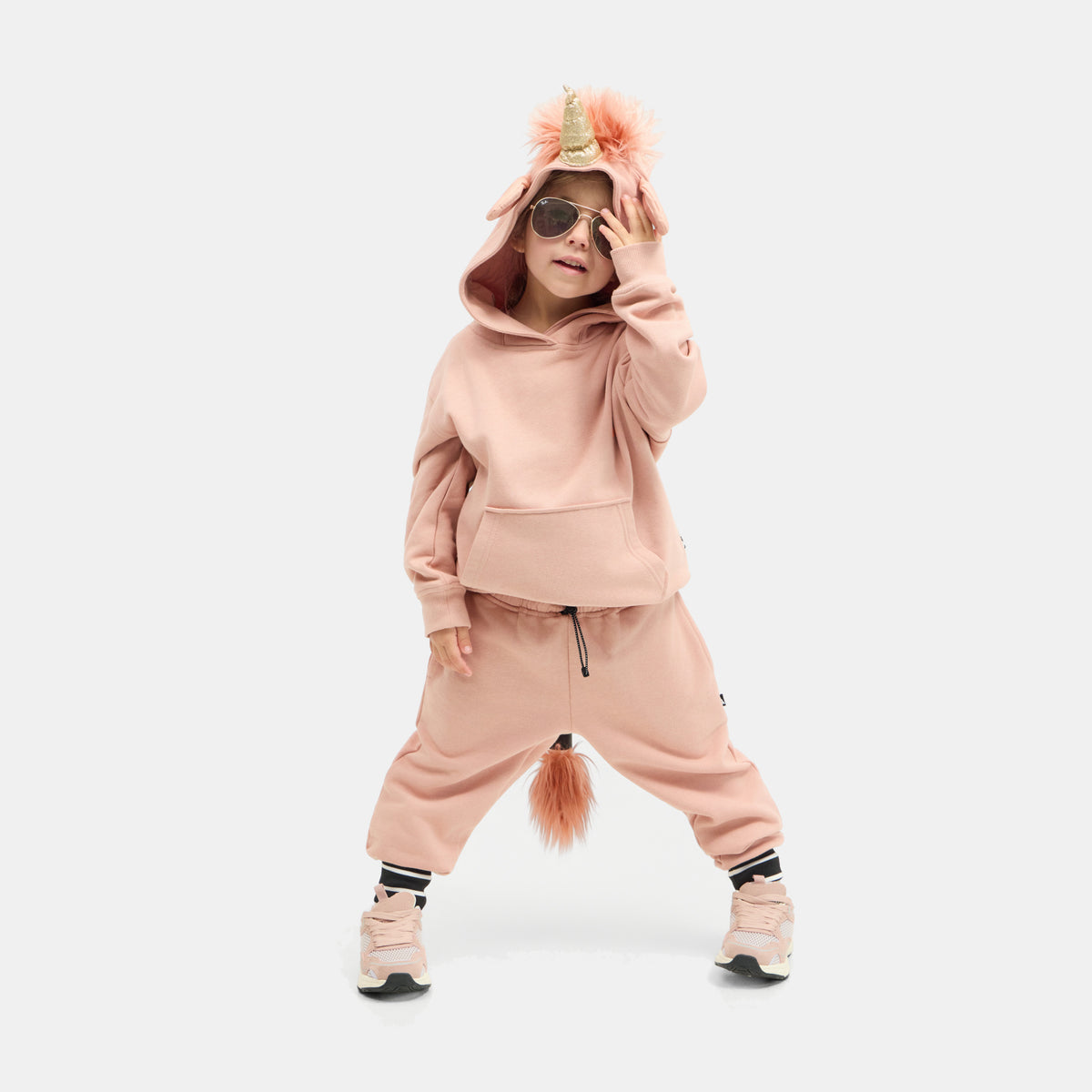 Child standing in the dusty pink UNIDO Sweatsuit, hood up with the glitter unicorn horn and faux-fur mane.