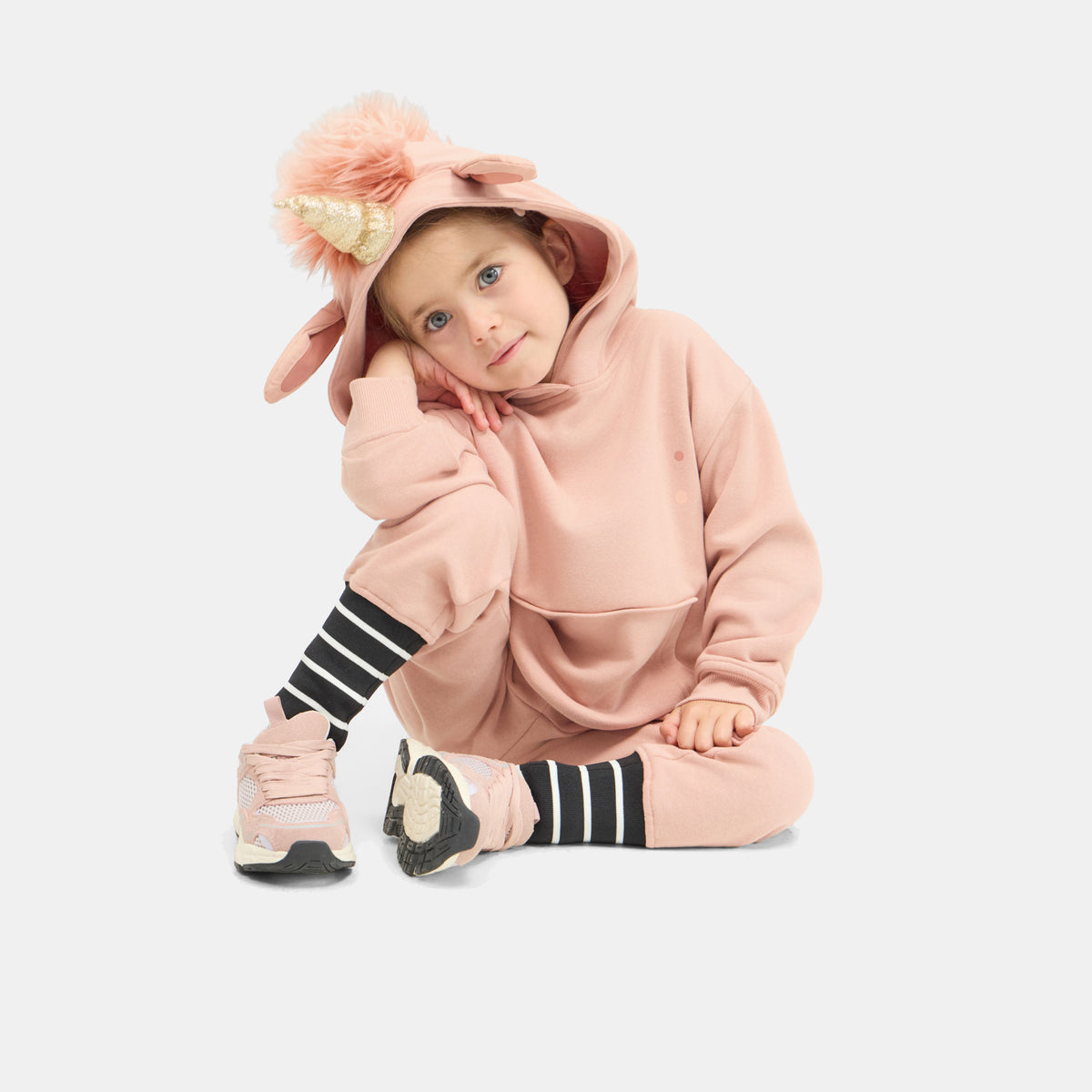 Child kneeling in the UNIDO Sweatsuit, hood up with the unicorn horn and mane.