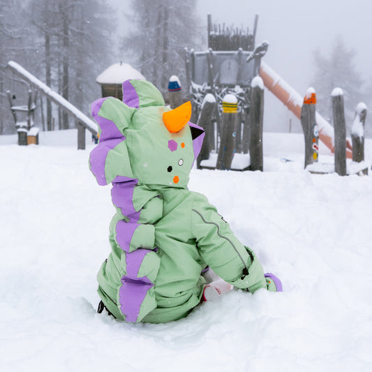 Child sitting in snow in the LILIDO Mint Snowsuit, back view showing the dino spikes